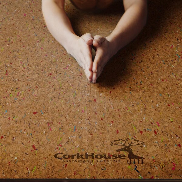A person poses on a cork yoga mat with a bright confetti pattern on the top of the mat.